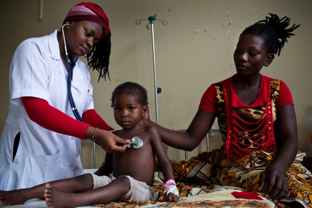 A health worker examines a young child as his mother looks on.