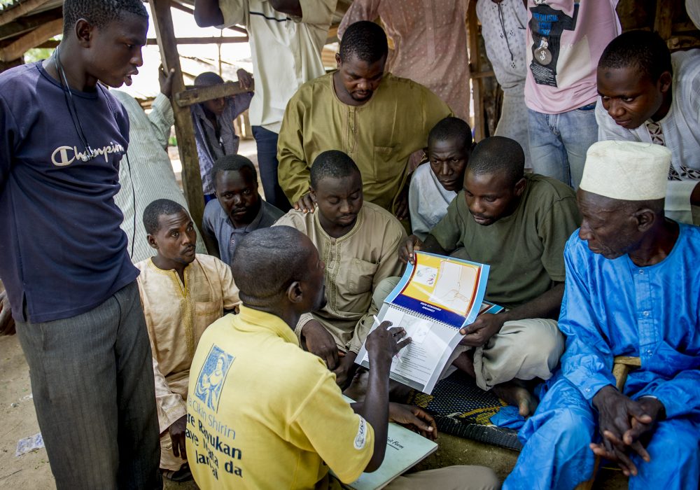 A male motivator uses a booklet to talk to a group of men about family planning.