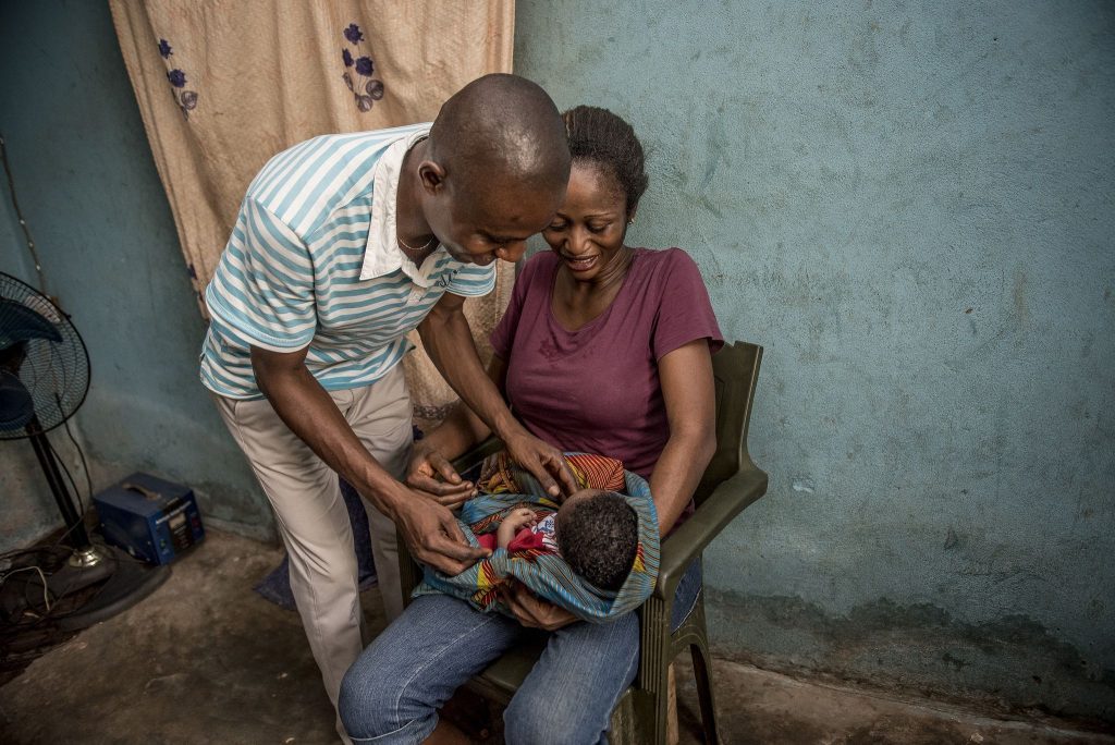 Woman sitting and holding baby with man standing