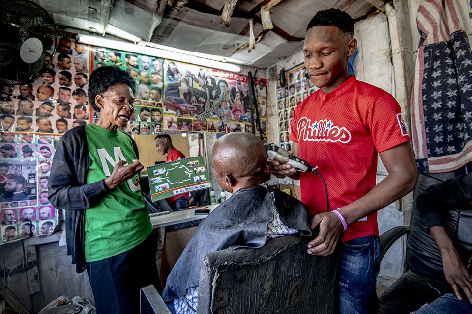 Woman explaining something to man sitting in barber chair while male hair stylist shaves the man's head