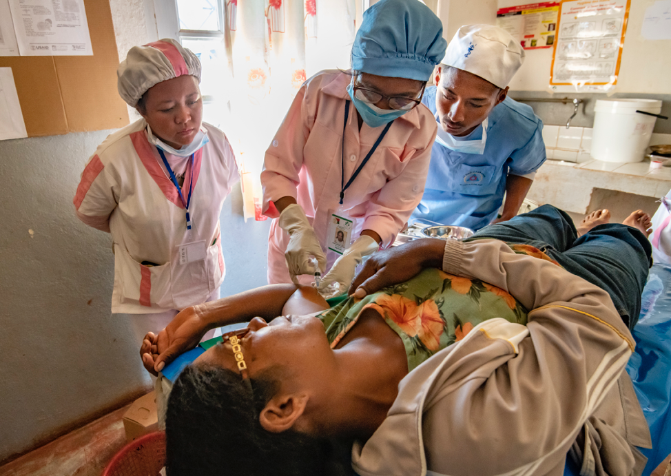 Three medical providers standing over woman laying on table