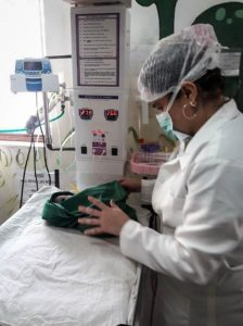 Female pediatrician wearing mask providing care to newborn laying on exam table.