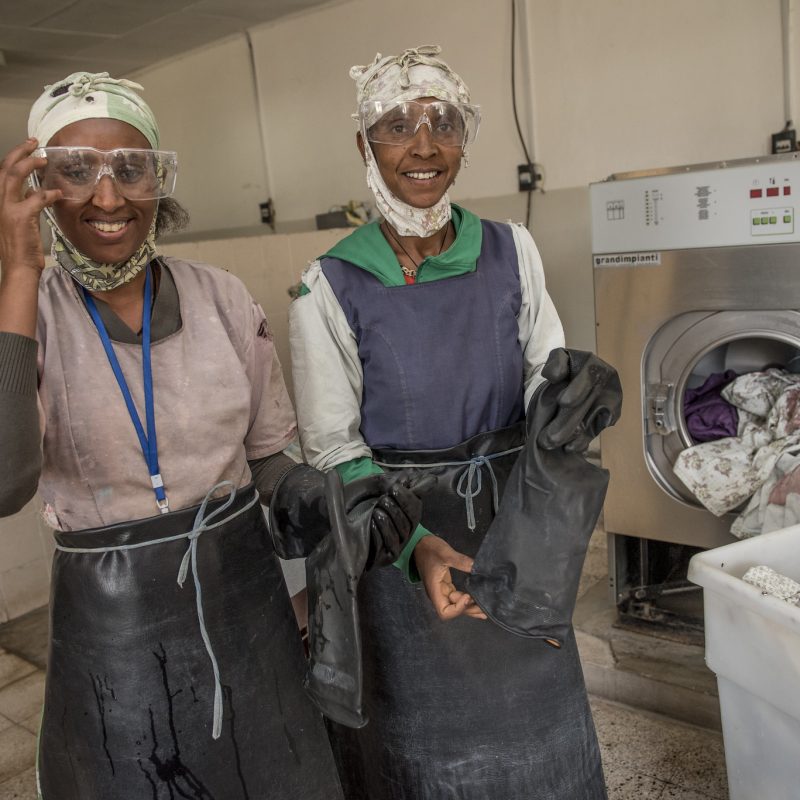 Two women standing near an industrial size washing machine.