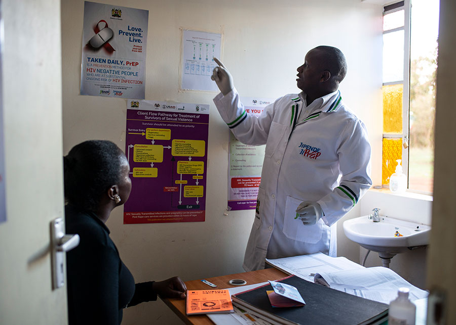 Clinician gesturing toward a wall chart while a patient observes